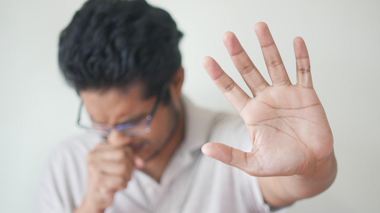 Uomo che tossisce e tende il braccio sinistro, con primo piano sulla mano