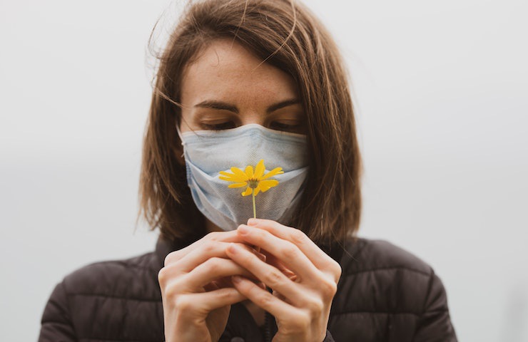 Donna indossa una mascherina sulla faccia e tiene un fiore in mano