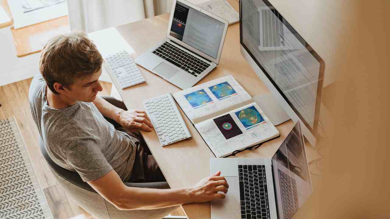 Ragazzo che lavora contemporaneamente con tre computer connessi a internet