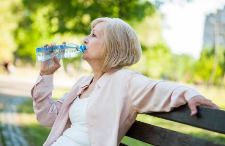 Donna anziana che beve una bottiglia d'acqua al parco