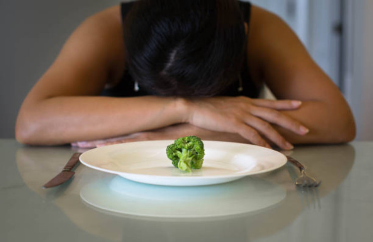 Ragazza a dieta afamata e disperata davanti a un piatto con un broccolo