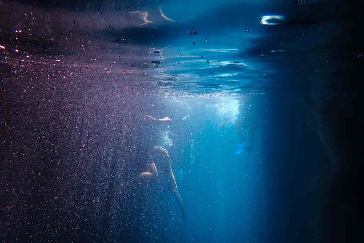 Persona in mare vista da sotto al pelo dell'acqua con raggi colorati di luce che entrano in mare