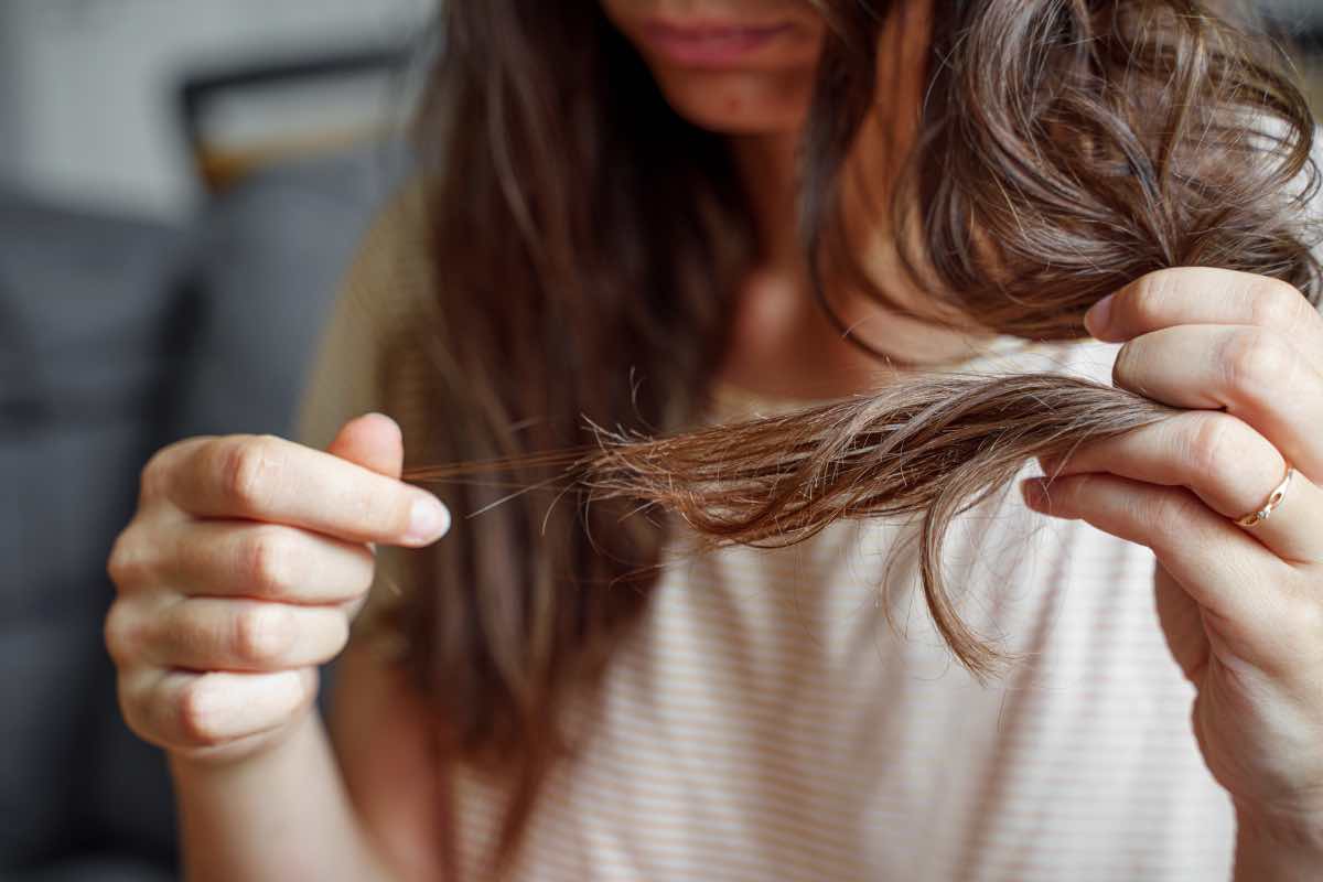 Una ragazza s guarda le punte dei capelli sfilacciati