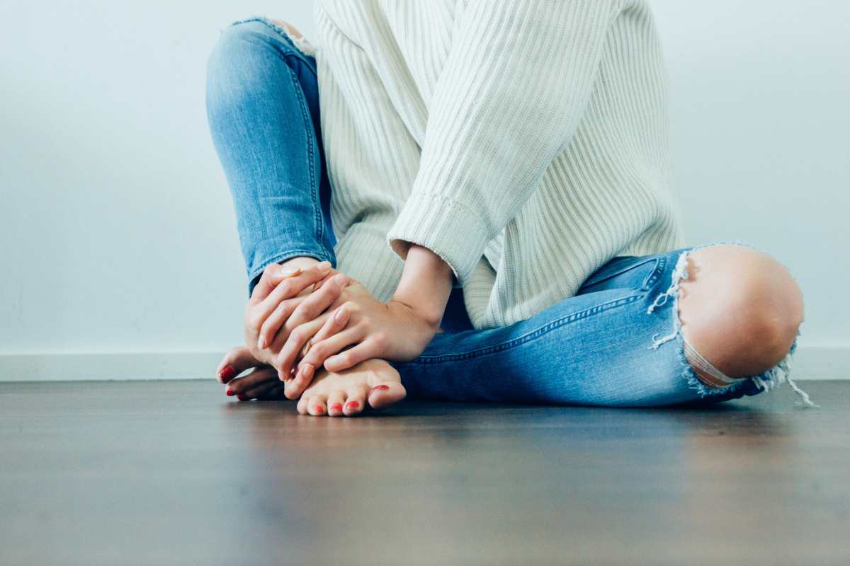 Ragazza in jeans che si tiene la caviglia per il dolore