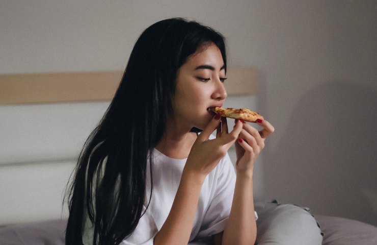 Ragazza colpita da fame nervosa notturna mangia una pizzetta a letto