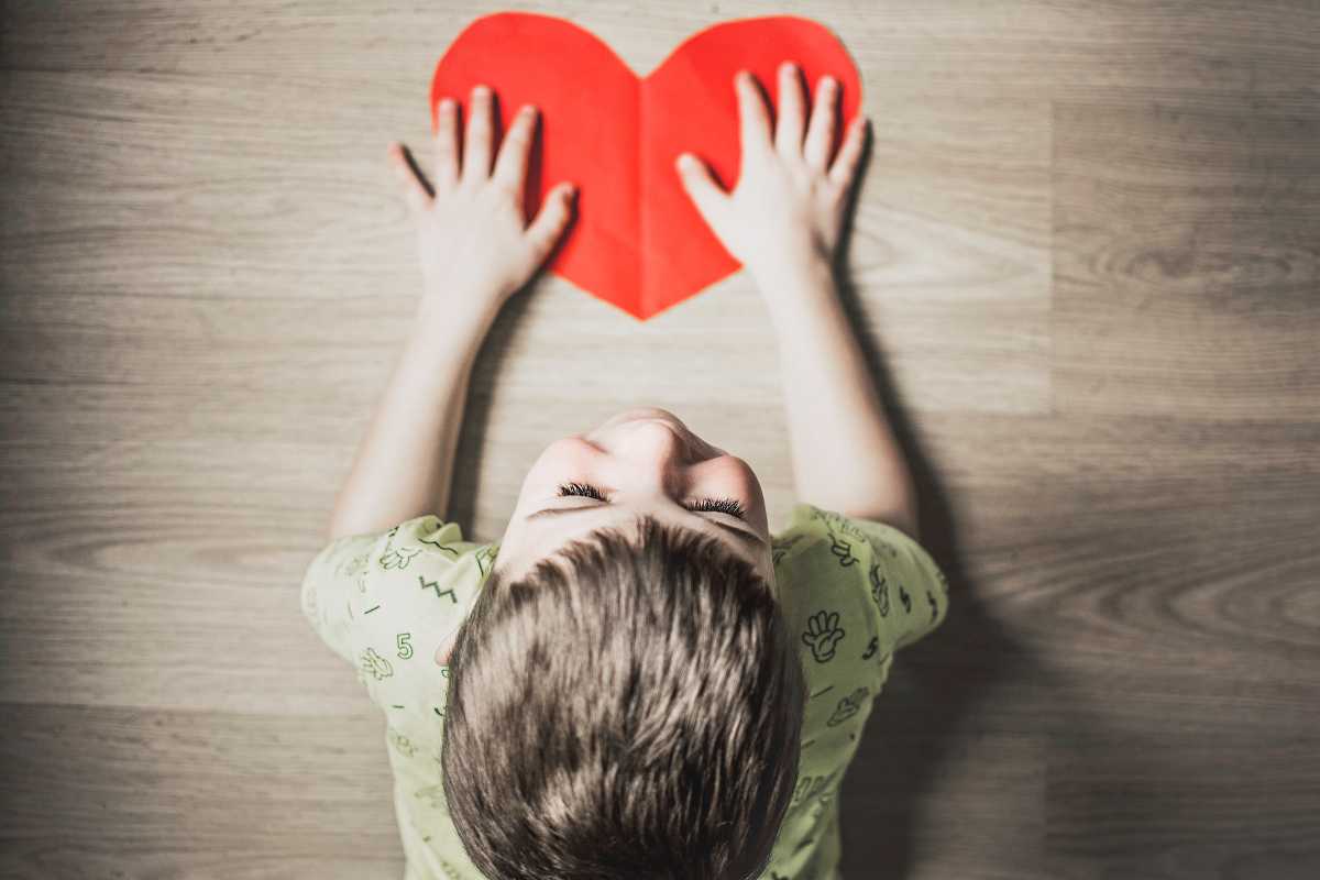 Bambino sul pavimento con un cuore di carta in mano